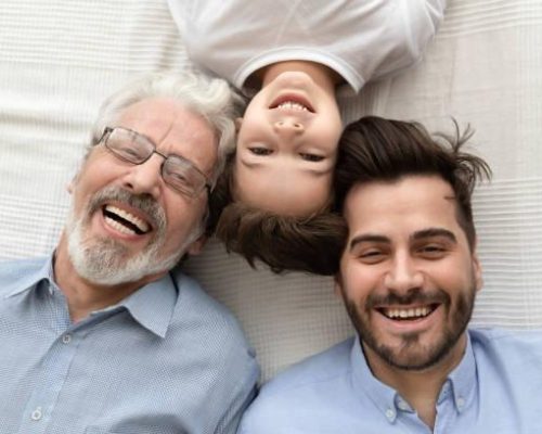 Top view of happy three generations of men lying on bed looking at camera making photo together, portrait of smiling little son, father and grandfather posing for picture laughing relaxing at home